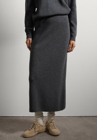 Falda maxi de punto gris oscuro con una textura acanalada, combinada con zapatillas beige y calcetines de color claro. Diseño minimalista, acabado suave.