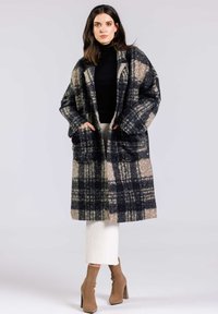 Manteau long à carreaux dans des tons bleu foncé, beige et gris. Texture douce, forme oversize, avec de grandes poches et une coupe décontractée.