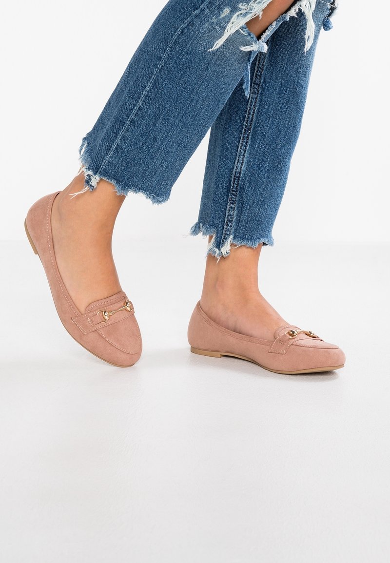 Mocassins en daim rose avec bout rond et détail en métal doré. Portés avec un jean bleu délavé effiloché pour un look décontracté.