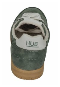 Groene suède sneaker met een witte gewatteerde kraag, voorzien van een rubberen zool en een prominent "HUB" logo op de hiel. Geweven oppervlaktedetail.