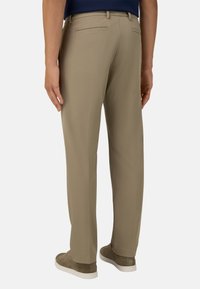 Béžové kalhoty s přímým střihem, dvěma zadními kapsami a jemnou strukturou. V kombinaci se světle šedými teniskami pro neformální vzhled.