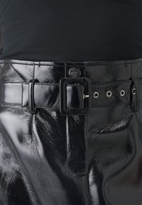 Svart, glänsande läderbyxor med ett brett bälte som har en fyrkantig spänne och flera metalldetaljer. Slät textur och elegant design.