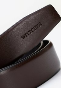 Brązowy skórzany pasek z teksturowanym wykończeniem i wytłoczonym logo "WITTCHEN". Pasek jest zwinięty, ukazując swoje gładkie krawędzie.
