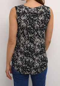 Top sin mangas en blanco y negro con un diseño estampado, cuello redondo y dobladillo curvado. Combinado con jeans azules.