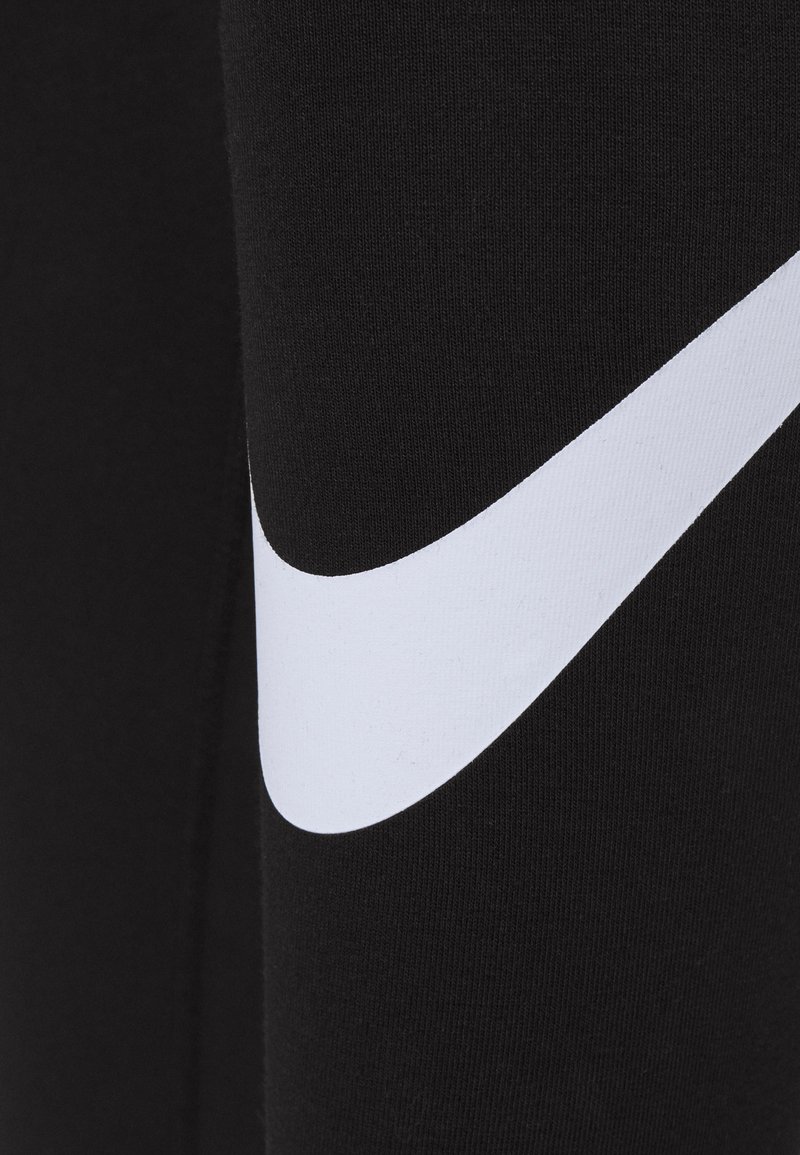 Un tissu noir au toucher lisse présente un grand logo swoosh blanc de Nike. Le design est moderne et minimaliste, mettant l'accent sur le contraste.