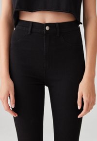 Jeans neri a vita alta in denim, con chiusura a bottone frontale, due tasche anteriori e una texture liscia.