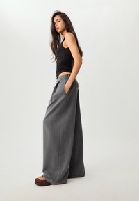 Czarny top bez rękawów z marszczeniami, w połączeniu z szarymi spodniami o wysokim stanie i szerokich nogawkach, które mają boczne kieszenie i gładką teksturę.