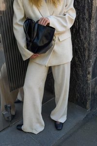 Krēmkrāsas teksturēta uzvalka bikses ar brīvām kājām un pielāgotu žaketu. Melnas ādas soma ar rokturiem, valkāta ar melniem norādītiem apaviem.