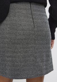 Jupe à motif pied-de-poule en tissu noir et blanc, avec une coupe droite, une texture subtile et une couture au dos pour un aspect ajusté.