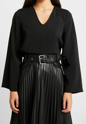 Black long-sleeve blouse with a V-neck, paired with a high-waisted black pleated faux leather skirt and a wide belt with a silver buckle.