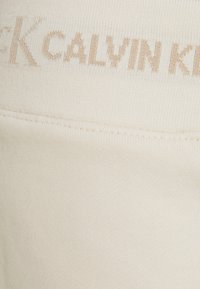 Calvin Klein krémová textilie ze směsi bavlny s ribbed texturou, sešité logo v světle béžové barvě. Hladký, bezšvový design.