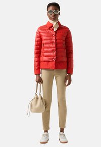 Rode gewatteerde jas met een kraag en drukknopen, gecombineerd met beige broek, witte sneakers en een crèmekleurige bucketbag.