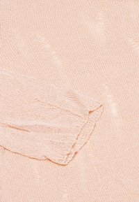 Lichtroze gebreide trui met een textuurpatroon van verhoogde lijnen en een ribbelmanchet. Het materiaal lijkt zacht en lichtgewicht te zijn.
