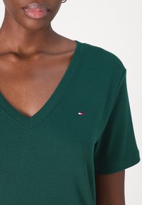 Grön V-ringad t-shirt i mjuk bomull, med korta ärmar och en liten logotyp i röd, blå och vit på bröstet.