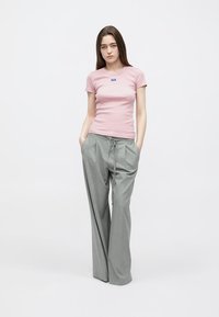 T-shirt aderente rosa chiaro con un piccolo logo blu, abbinata a pantaloni larghi grigio chiaro con coulisse in vita.