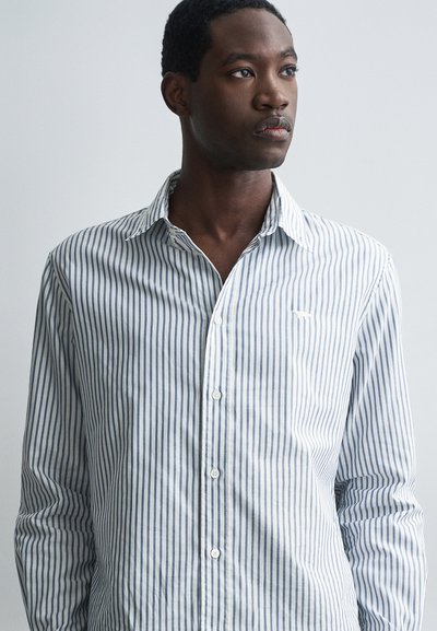 Camisa de manga larga a rayas en algodón azul claro y blanco. Presenta un cuello abotonado y un pequeño logo bordado en el pecho.