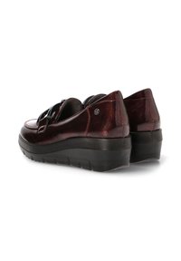Zapatos de charol burdeos con suelas negras, diseño de corte bajo, parte trasera resistente y correa decorativa. Presentan un sutil logo en el lateral.