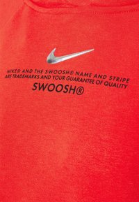Logo Nike swoosh argenté au-dessus d’un texte noir sur tissu rouge indiquant que les marques Nike garantissent la qualité, avec le mot SWOOSH en gras.