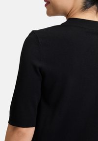 Top corto a maniche corte in maglia nera. Texture liscia con scollo rotondo e design aderente. Cuciture visibili sulle spalle e sulla schiena.