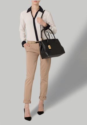 Schwarze Lederhandtasche mit goldenen Akzenten, beiger Hose und weißer Bluse mit schwarzen Akzenten. Schwarze High-Heels.