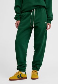 Gröna sweatpants med elastiska muddar, dragsko i midjan och liten logotypdetalj. Matchat med gula sneakers med blå detaljer.