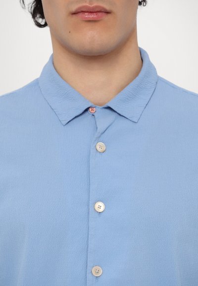 Camicia azzurra a maniche corte con tessuto strutturato, colletto button-down e tre bottoni di diverse tonalità sul davanti.