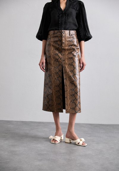 Bruine leren midi-rok met slangenpatroon en een split aan de voorkant. Zwarte blouse met textuurdetails. Crème sandalen met blokhak en strikaccenten.