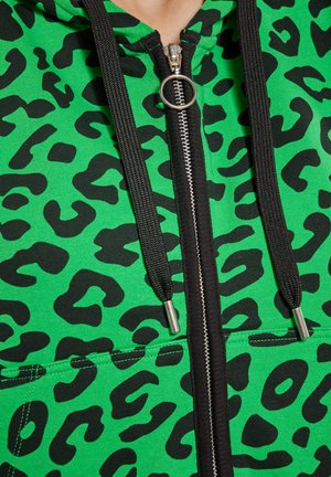 Hanorac verde cu imprimeu de leopard negru, prevăzut cu un fermoar argintiu, șnururi negre și buzunar frontal. Material texturat.