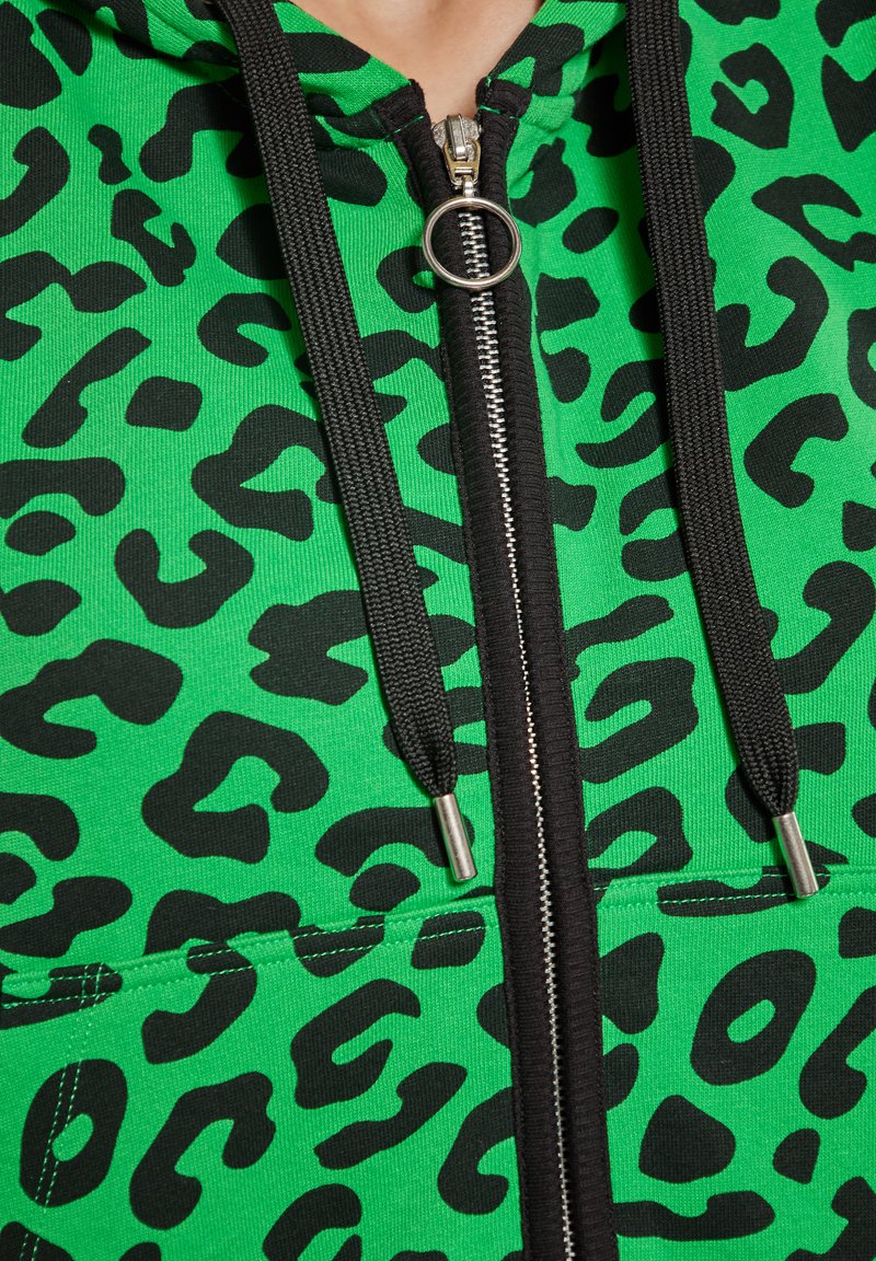 Felpa verde con stampa leopardata nera, dotata di una zip argentata, corde nere e tasca frontale. Tessuto testurizzato.