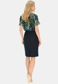 Bluzka w kwiaty w ciemnych kolorach z krótkimi rękawami, w połączeniu z dopasowaną granatową spódnicą ołówkową z rozcięciem z tyłu i beżowymi szpilkami.