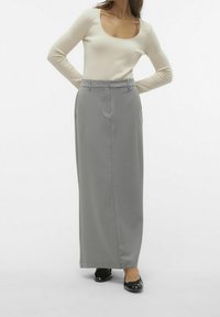 Lång grå kjol med skräddarsydd passform, med hög midja och rak silhuett, kombinerad med en krämfärgad långärmad topp och svarta platta skor.