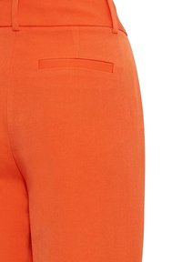 Pantaloni arancioni con una texture liscia, caratterizzati da una tasca posteriore e una vestibilità su misura. La cintura è in tinta con il colore del tessuto.