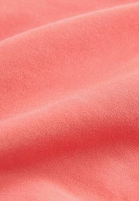 Korálová tkanina, měkká textura, hladký povrch a jemný lesk. Materiál vykazuje jemné tkaní s mírnými záhyby a konturami.