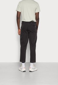 Pantalones negros recortados con un ajuste relajado y cintura elástica, combinados con una camiseta verde claro y zapatillas blancas con detalles.