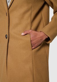 Brun ullrock med slät yta, utrustad med sidoficka och två mörka knappar. Enkel design med skräddarsydd passform.