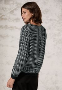 Maglione a righe bianche e nere con design geometrico, tessuto morbido, maniche lunghe e scollatura arrotondata. Presenta un orlo a coste.