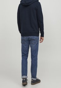 Námořnická mikina s kapucí a klokankou, spárovaná s modrými džínami a tmavými teniskami, ukazující ohrnuté manžety a ševové detaily.