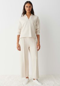 Crèmewitte, ontspannen-fit trui met een kraag, gecombineerd met wijde, bijpassende broek en witte sneakers. Soepele textuur.