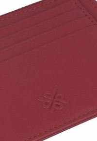 Red leather cardholder with four slots, smooth texture, and embossed logo on the front. Neat stitching along the edges.