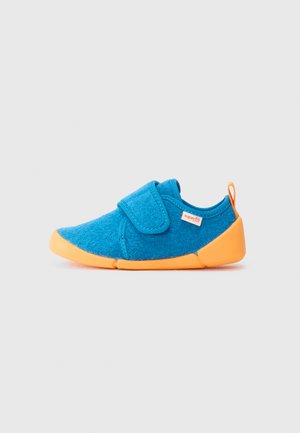 Blauwe vilten schoen met een oranje rubberen zool, voorzien van een klittenbandsluiting en een klein identificatielabel aan de zijkant. Rond ontwerp van de neus.