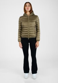 Giacca verde oliva imbottita con cappuccio, chiusura con zip e cuciture orizzontali, abbinata a pantaloni neri e sneakers bianche.