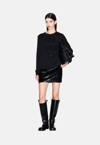 Sudadera negra con letras texturizadas "GIORGIO", combinada con una mini falda negra con lentejuelas, botas negras hasta la rodilla y un bolso negro.