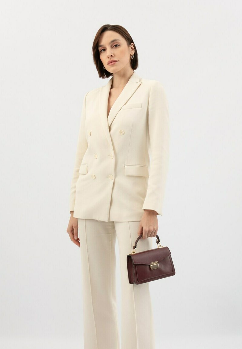 Lichtbeige dubbelzijdige blazer met bijpassende broek; handtas in diep bordeauxleer met gouden hardware en een bovenhandvat.