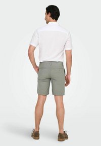 Chemise blanche à manches courtes avec un dos texturé et un short vert avec des poches arrière. Chaussures en cuir marron à lacets complètent la tenue.