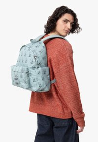 Ljusblå ryggsäck med ett upprepat Snoopy-mönster, tillverkad av slitstarkt tyg, med en framficka och vadderade axelremmar.