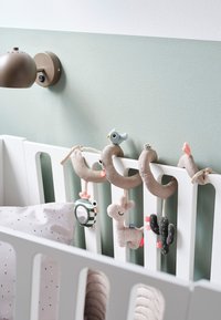 Zachte pluchen mobiel met beige lussen, een blauwe vogel, grijze cactus en een pluchen hert, hangend tegen een muntgroene muur boven een wit ledikant.