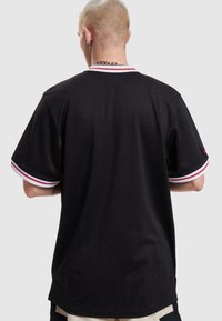 Tricou negru cu mânecă scurtă, dintr-un material cu textură tip plasă. Are un guler ribbed cu dungi roșii și albe și un detaliu subtil al logo-ului pe lateral.