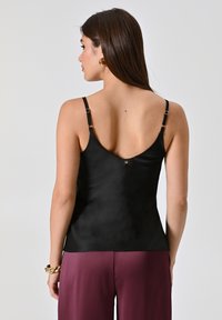 Camisole nera in satin con spalline sottili regolabili e schiena bassa. Dettagli notevoli includono accenti in metallo dorato e una texture liscia.