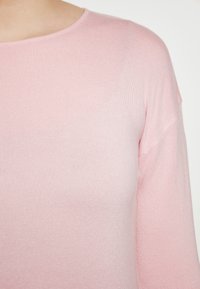 Helles rosa gestricktes Sweatshirt mit rundem Halsausschnitt und langen Ärmeln. Die Textur ist glatt mit einem gerippten Design. Keine bemerkenswerten Muster oder Akzente.