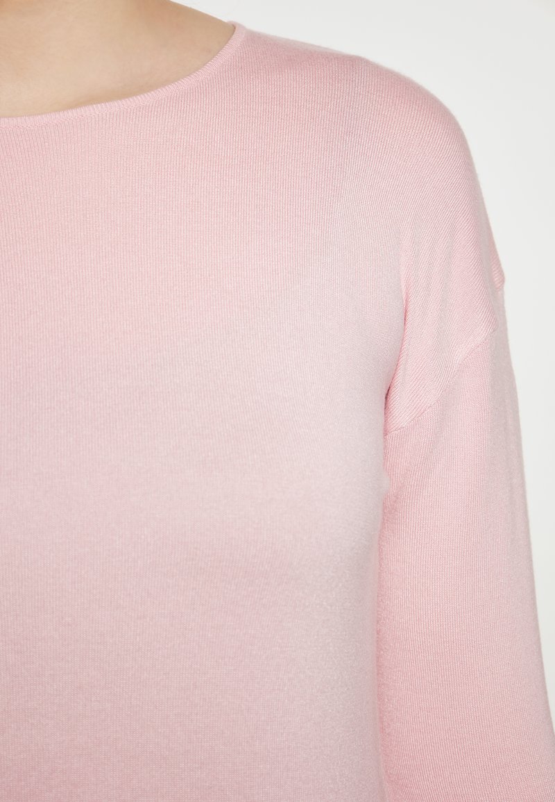 Helles rosa gestricktes Sweatshirt mit rundem Halsausschnitt und langen Ärmeln. Die Textur ist glatt mit einem gerippten Design. Keine bemerkenswerten Muster oder Akzente.